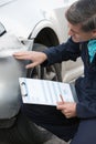 Auto Workshop Mechanic Inspecting Damage To Car And Filling In R