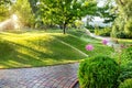 Automatic garden watering system with different sprinklers installed under turf. Landscape design with lawn hills and fruit garden