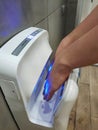 In a hand dryer in a public restroom, a man dries his hands after washing