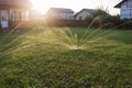 Automatic sprinkler system watering the lawn on the background of countryside houses on the sunset Royalty Free Stock Photo