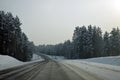 Automobile asphalt road runs along a dense snow-covered forest. Winter landscape. Evening lighting.