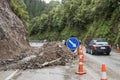 Automobile car driving past rockflall, rocks, landslide debris, traffic cones and warning signs on roadway highway. Dangerous road