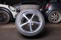 Automobile composition made up stack of tires and wheel with shiny metal disc in the foreground against the background of cars in