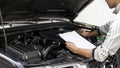 Automobile mechanic repairman checking a car engine with inspecting writing to the clipboard the checklist for repair machine, car