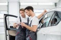 Automobile mechanics checking checklist while standing by car in workshop