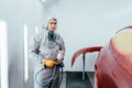 Automobile repairman painter hand in protective glove with airbrush pulverizer painting car body in paint chamber. Royalty Free Stock Photo