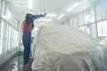 Automobile repairman painter in protective workwear and respirator painting car body in paint chamber. Automobile repair. Car