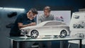 Automotive engineers discuss car design making corrections in sculpture of a car