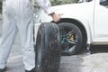 Automotive mechanic man in white uniform carrying spare tire preparing change a wheel of car. Auto repair service. Royalty Free Stock Photo