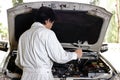 Automotive mechanic in uniform with wrench diagnosing engine under hood of car at the repair garage. Royalty Free Stock Photo