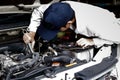 Automotive mechanic in uniform with wrench diagnosing engine under hood of car at the repair garage. Royalty Free Stock Photo