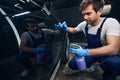 Auto repair shop worker spraying car with degreasing liquid