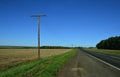 The automotive side of the paved road. Telegraphic wooden poles and a sloping field along the road. Royalty Free Stock Photo