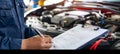 Automotive technician preparing job checklist at open car engine for repair evaluation Royalty Free Stock Photo