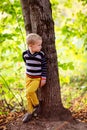Autumn baby boy stands near a tree, looking back forest