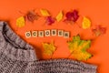 Autumn background with leaves and a warm sweater, the word `October` is made of wooden letters on an orange background.