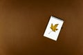 Autumn busines concept - blank ring-bound notebook with golden maple leaf and pen on brown background with copy space Royalty Free Stock Photo