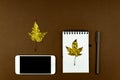 Autumn busines concept - blank ring-bound notebook with golden maple leaf, white smartphone and pen on brown background with copy Royalty Free Stock Photo