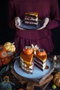 Autumn cake with persimmon and caramel with a pumpkin and a girl in a burgundy dress on a black background, Atmospheric dark food