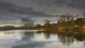 Autumn city landscape trees with colorful foliage are reflected in the river against a cloudy sky lit by the rays of sunset Royalty Free Stock Photo