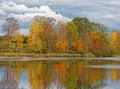 Fall colors orange, yellow and red in trees at pond edge with reflections in water