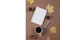 Autumn composition. Golden maple leaves, coffee cup, bumps, notebook and pen on brown background. Autumn or Winter concept. Royalty Free Stock Photo