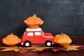 Autumn composition with red toy car and orange pumpkins on leaves and wooden background