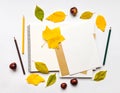 Autumn composition with sketchbook and pencils, decorated with yellow and green leaves. Flat lay, top view