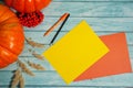 Two orange pumpkins, two sheets of blank paper, a pen and pencil, Rowan berries and dried cereals on a light blue wooden backgroun