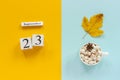 Autumn composition. Wooden calendar September 23, cup of cocoa with marshmallows and yellow autumn leaves on yellow blue Royalty Free Stock Photo