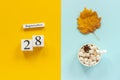 Autumn composition. Wooden calendar September 28, cup of cocoa with marshmallows and yellow autumn leaves on yellow blue Royalty Free Stock Photo