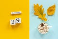 Autumn composition. Wooden calendar September 29, cup of cocoa with marshmallows and yellow autumn leaves on yellow blue Royalty Free Stock Photo