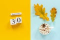 Autumn composition. Wooden calendar September 30, cup of cocoa with marshmallows and yellow autumn leaves on yellow blue