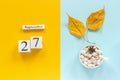 Autumn composition. Wooden calendar September 27, cup of cocoa with marshmallows and yellow autumn leaves on yellow blue Royalty Free Stock Photo