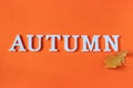 Autumn composition. Word Autumn from white letters and bright yellow oak leaf on orange paper background. Concept Hello fall.