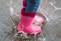Autumn concept. The girl in pink boots jumping in puddles after rain outdoors.