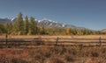 Autumn country landscape with a fence, snowy mountains and forest