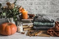 Autumn cozy home still life. Pumpkin, stack of books, burning candle, pile of winter autumn sweaters, jar of marshmallows on the