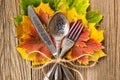 Autumn dinner place setting for Thanksgiving holiday with colorful maple leaves on rustic wooden boards