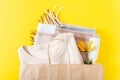 Autumn discount and sale concept. Paper shopping bag, yellow flowers and knitted sweater on a bright yellow background. Flat lay.