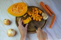 Autumn dishes, pumpkin soup cooking.Female hands are cutting a pumpkin on a wooden plank, onions, ginger and carrots