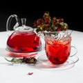 Autumn evening teatime with splash in red herbal tea cup, transparent tea pot with hawthorn berries, rose hip, dry leaves on white Royalty Free Stock Photo