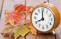 Autumn fall concept, alarm clock with red leaves on a wooden background
