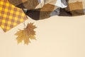 Autumn, fall concept. Checked orange gift paper bag, warm cozy blanket plaid, autumn dried leaves on pastel beige background. Flat Royalty Free Stock Photo