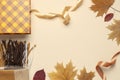 Autumn, fall concept. Checked orange gift paper bag, warm cozy blanket plaid, autumn dried leaves, holiday ribbons on pastel beige Royalty Free Stock Photo