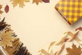 Autumn, fall concept. Checked orange gift paper bag, warm cozy blanket plaid, autumn dried leaves, holiday ribbons on pastel beige Royalty Free Stock Photo