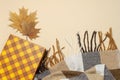 Autumn, fall concept. Checked orange gift paper bag, warm cozy blanket plaid, autumn dried leaves on pastel beige background. Flat Royalty Free Stock Photo