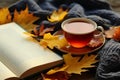 Autumn, fall leaves, cup of tea, opened book and warm scarf on wooden table. Seasonal, book reading, Sunday relaxing, teatime and