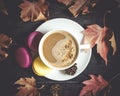 Autumn, fall leaves, hot steaming cup of cappuccino coffees, macaroons, cones on wooden table background. Royalty Free Stock Photo