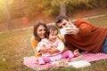 Autumn family picnic on grass smiling and making selfie